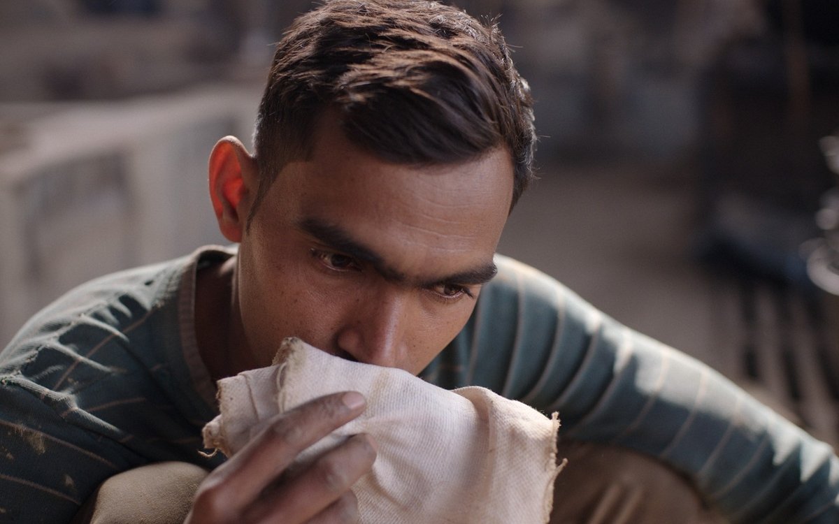 A young man holds a piece of cloth to his face and smells it