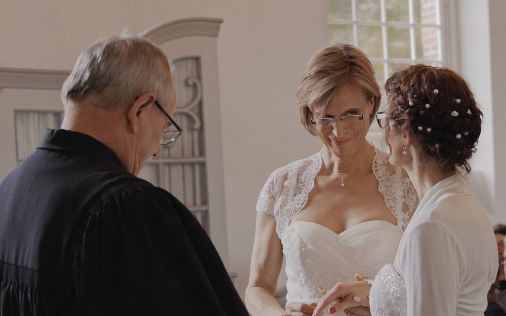 A pastor stands before two brides at a wedding in a church