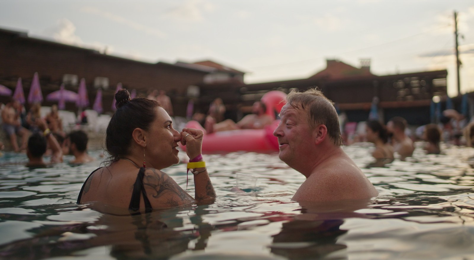 Two people talk in a crowded outdoor pool with an inflatable flamingo behind them