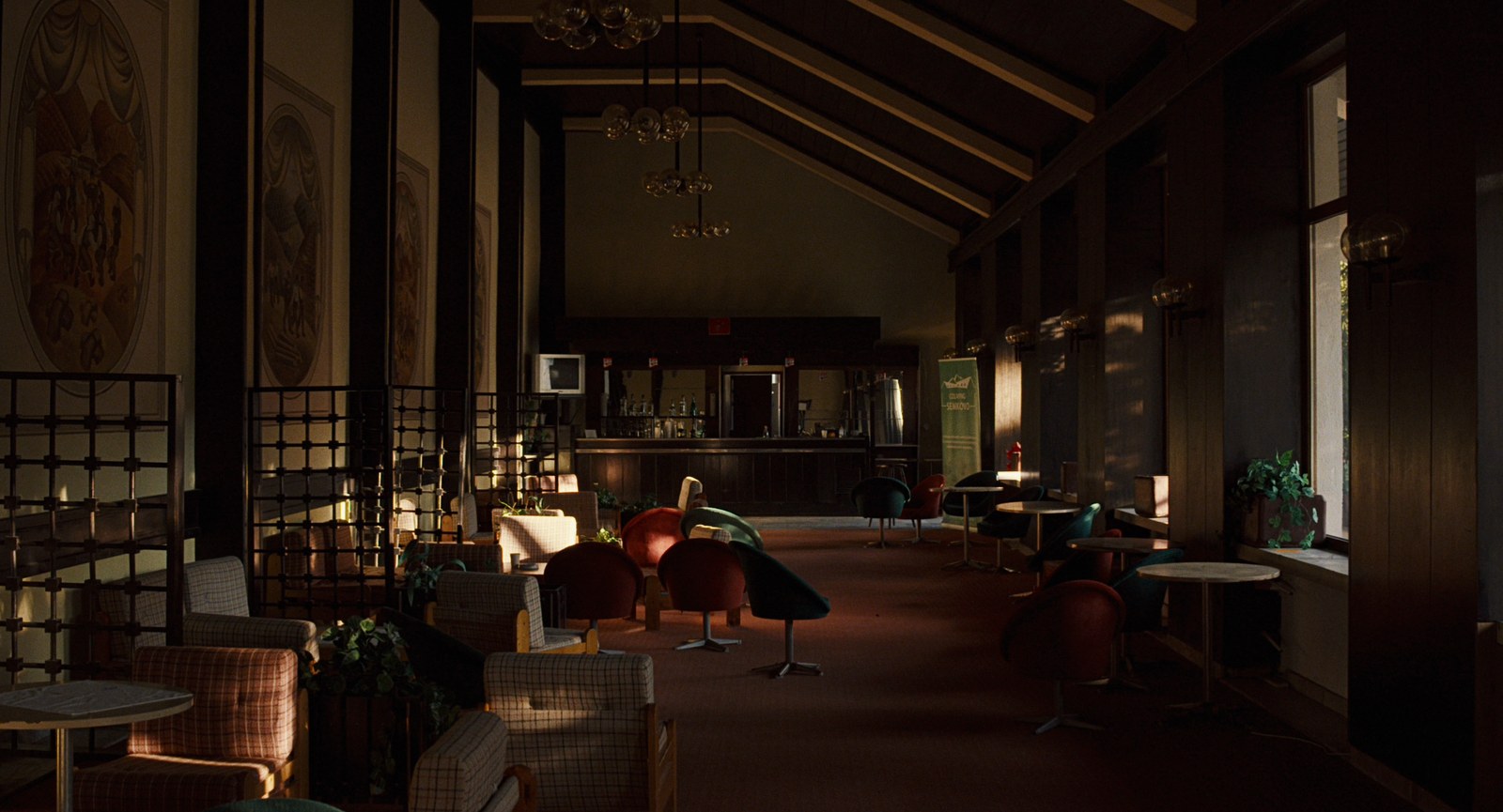 A long, dim hotel hall with armchairs, round tables and a wooden ceiling