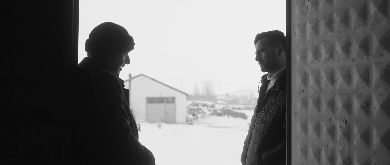Two men talk in a doorway, a snowy farmyard behind them