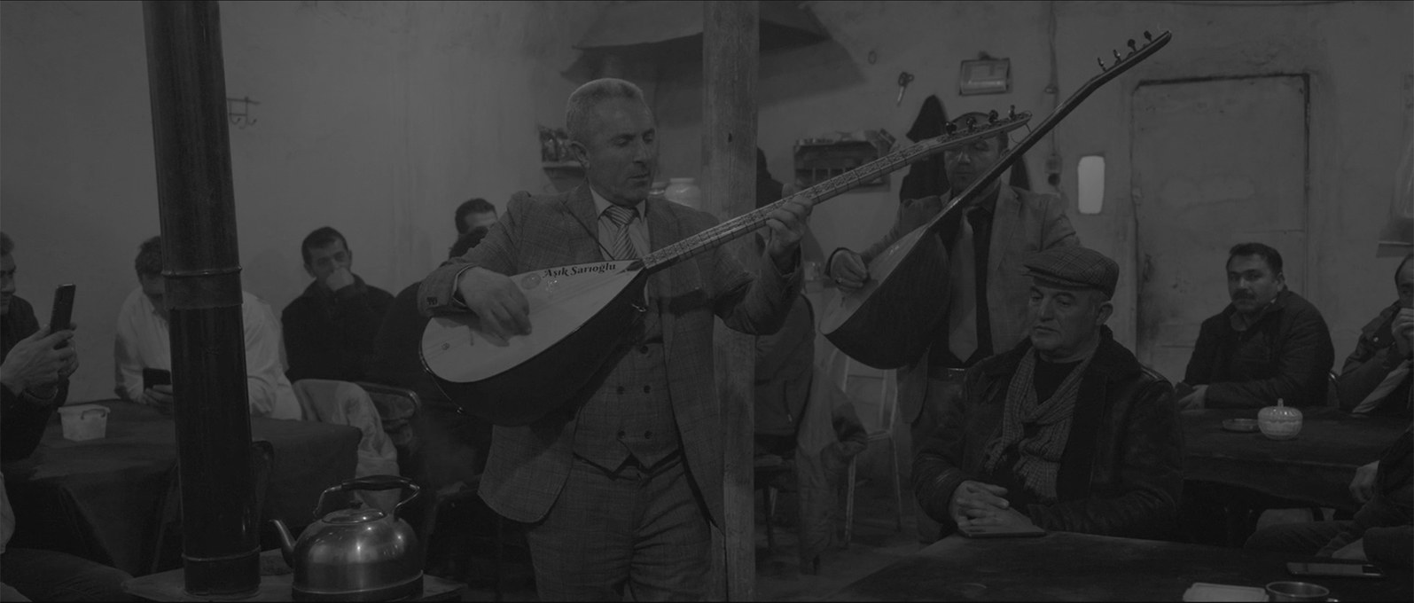 A musician plays the saz in a crowded village tea house