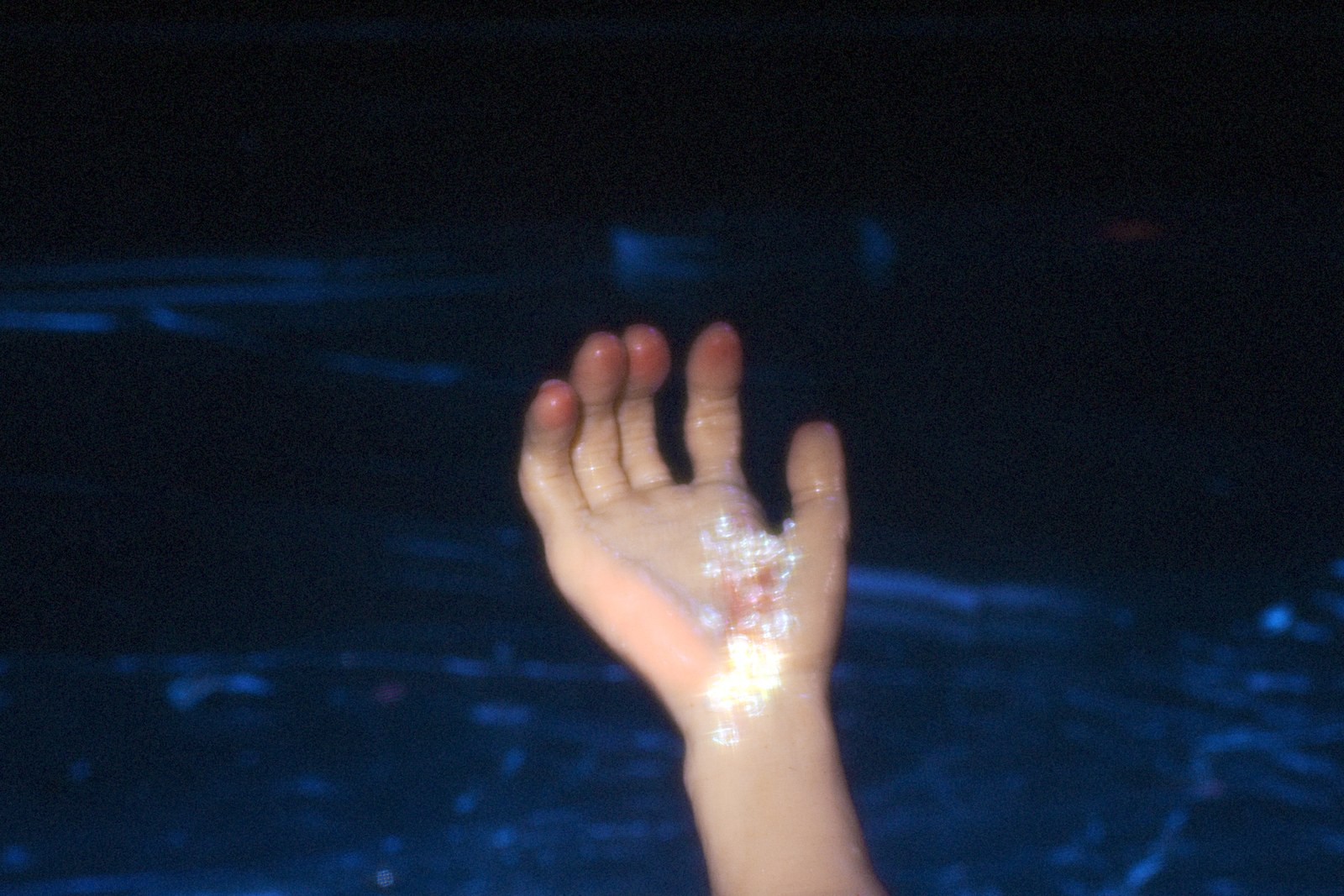 A sparkling puppet hand reaches up against dark blue water