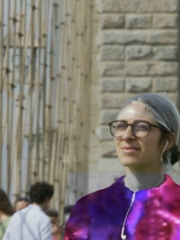 A woman in a colourful jacket in front of a stone building