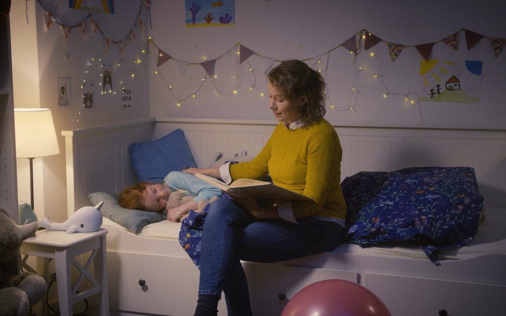 A mother reads to a child lying in bed in a decorated bedroom
